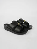 Black sandals with gold buckles on a light gray background