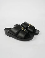 Black sandals with gold buckles on a light gray background